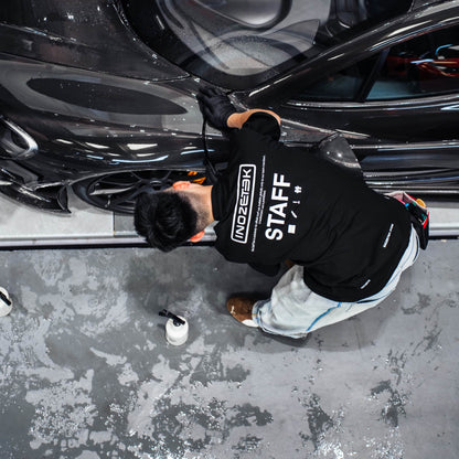 Person in a black 'Staff' sweatshirt working on a black car in a garage.