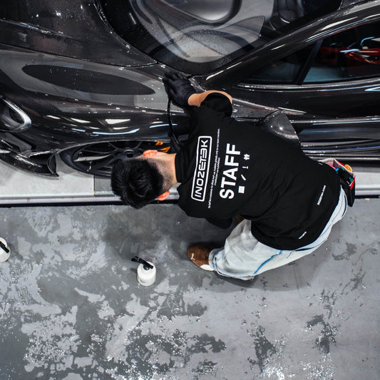 Person in a black 'Staff' sweatshirt working on a black car in a garage.